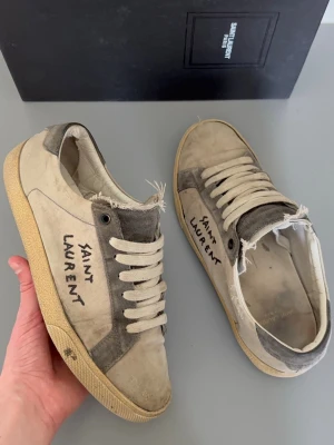 Saint Laurent skor - Snygga sneakers från Saint Laurent i beige och grå mocka och canvas med slitna detaljer och råa kanter. Klassisk låg modell med vit sula och handskriven logga på sidan. Perfekta för en avslappnad och trendig streetstil. Ingen box! Storlek 40
