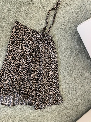 Leopardmönstrad kortkjol med volang - Säljer en snygg kortkjol med leopardmönster och volangkant. Kjolen har omlottmodell med knytband i midjan och är gjord i ett lätt, luftigt material som passar perfekt till varma dagar. Perfekt för dig som vill sticka ut lite extra!