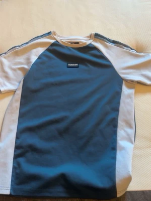 Blå och vit t-shirt från McKenzie - Snygg t-shirt från McKenzie i blått med vita paneler längs sidorna och ärmarna. Klassisk passform med rund hals och korta ärmar. Perfekt för en avslappnad stil.
