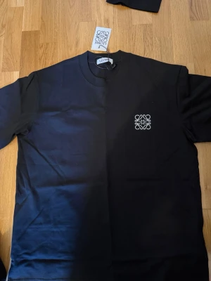 Svart t-shirt från Leowe med logga - Snygg svart t-shirt från Leowe med vit broderad logga på bröstet. Klassisk rund halsringning och korta ärmar. Perfekt basplagg med stilren design som passar till allt. Tillverkad i mjuk bomull för skön känsla hela dagen.