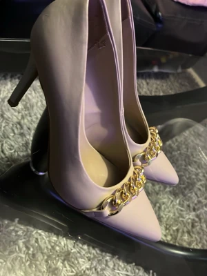 Beige pumps med guldkedja Graceland - Snygga beige pumps från Graceland med spetsig tå och hög klack. Skorna har en dekorativ guldfärgad kedja framtill som ger en trendig touch. Tillverkade i ett slätt material som ger en stilren look.