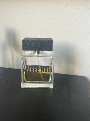 Ambre Noir parfym från Yves Rocher - Ambre Noir parfym från Yves Rocher i en stilren, rektangulär glasflaska med svart fyrkantigt lock. Flaskan har tydlig svart text på framsidan och innehållet är bärnstensfärgat. Perfekt för dig som gillar eleganta och maskulina dofter.