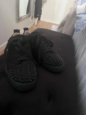Svarta sneakers med nitar - Säljer ett par svarta sneakers med coola svarta nitar på tån och ovandelen. Skorna har snörning och en klassisk låg siluett. Insidan är ljusbeige och materialet ser ut att vara mocka eller liknande tyg. Perfekta för dig som vill sticka ut lite extra. De är äkta men jag trodde att pappret där det stod att de var äkta var kvitto så jag slängde det.