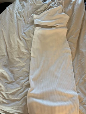 Vit ribbad långklänning H&M  - Säljer en vit ribbad långklänning från H&M Divided. Klänningen har smala axelband och en figurnära passform som framhäver siluetten. Perfekt för sommarens alla tillfällen och enkel att styla med accessoarer.