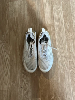 Vita Nike Air Max 270 sneakers - Snygga vita Nike Air Max 270 sneakers med mesh-ovandel och genomskinlig gul sula. Skorna har en sportig design med snörning och synlig Air Max-dämpning i hälen. Perfekta för dig som gillar streetwear och bekväma skor med modern look.