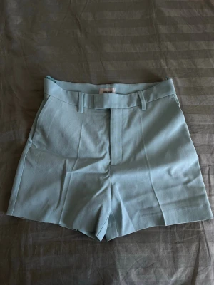 Zadig & Voltaire turkosa shorts - Säljer dessa fantastiskt fina Please Crêpe-shorts från Zadig & Voltaire i en elegant mintgrön/pastellblå nyans. Skräddad modell med stilrena detaljer och exklusiv känsla som passar perfekt till både vardag och mer uppklädda tillfällen. Shortsen är helt nya och oanvända med originaltags kvar. Den mjuka pastellfärgen är perfekt för vår- och sommargarderoben och är enkel att matcha med allt från skjortor och blusar till linnen och kavajer. Ett tidlöst och elegant plagg.