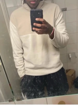 Beige och vit fleece tröja - Säljer en beige och vit fleece tröja med halv dragkedja och hög krage. Tröjan har en avslappnad passform och är perfekt för kyliga dagar. Materialet är mjukt och skönt mot huden. Enkel och stilren design som passar till det mesta.