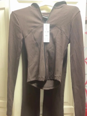 Brunt Gina Tricot Yoga Set  - Brun långärmad topp från Bershka med figurnära passform och dragkedja framtill. Toppen och byxorna är tillverkade i mjukt material, perfekt för en trendig och clean look. Helt oanvänt med prislapp kvar, nypris 720kr🌸