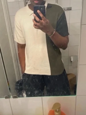 Tvåfärgad polotopp med dragkedja - Snygg polotopp i två färger, beige och mörkgrön, med halv dragkedja framtill. Toppen har korta ärmar och en stilren, sportig look. Perfekt för dig som gillar en clean och modern stil.