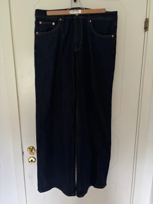 Mörkblåa wide leg jeans - Säljer ett par mörkblåa jeans med wide leg passform och låg till medel hög midja. Klassisk femficksmodell med kopparfärgade nitar och kontrastsömmar. Jeansen är tillverkade i kraftig denim och har raka, vida ben för en avslappnad look. Innerbenslängd: 76cm. Midjemått: 43cm
