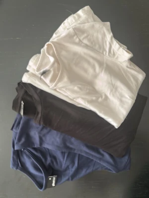 3 toppar från Gina st XS - Säljer 3 toppar från Gina Tricot i st XS. En blå långärmad med v-ringning, en svart kortärmad och en vit kortärmad.  