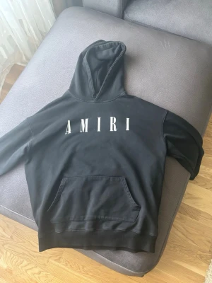 Svart hoodie från Amiri - Svart hoodie från Amiri med stor vit logga på bröstet. Klassisk modell med huva och känguruficka framtill. Tillverkad i mjukt bomullsmaterial, perfekt för en avslappnad och trendig streetwear-look