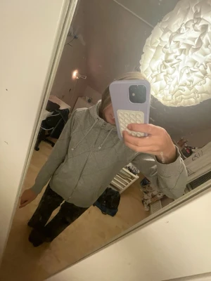 Ljusgrå hoodie med dragkedja - Säljer en ljusgrå hoodie med dragkedja framtill och två fickor. Hoodien har dragsko i huvan och ribbade muddar vid ärmsluten. Perfekt för chill dagar och enkel att matcha med det mesta. Materialet känns mjukt och bekvämt.