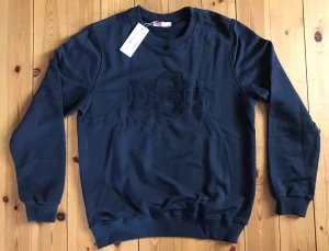 Mörkblå sweatshirt från Diesel - Mörkblå sweatshirt från Diesel med broderad DSL-logga på bröstet. Tröjan har rund halsringning, ribbade muddar vid ärmslut och nederkant samt en avslappnad passform. Perfekt för en casual och trendig look.