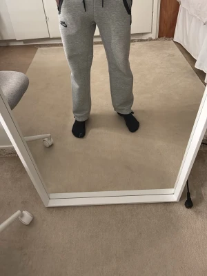 Gråa Nike mjukisbyxor med dragkedjor - Säljer ett par gråa mjukisbyxor från Nike med svarta detaljer. Byxorna har dragsko i midjan, dragkedjor vid fickorna och vid bensluten. Tillverkade i mjukt sweatshirtmaterial som är riktigt skönt. Perfekta för chill eller träning. Storlek XS men passar perfekt för S