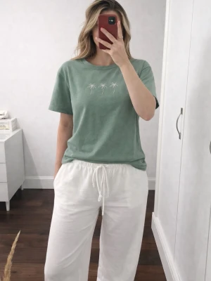 Grön t-shirt med palmtryck från SHEIN, strlk S - En grön t-shirt från SHEIN med dekorativt palmtryck framtill i storlek S (upplevs något liten i storleken). T-shirten är använd cirka 3 gånger och är i fint skick! Trycket är fastsytt i ett papp-liknande material (se bild 3) och är en del av designen, inte trasigt! Den är i 50% Bomull, 45% Polyester & 5% Elastan. Köptes för nypris 119kr! FÖRST TILL KVARN!