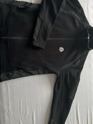Svart moncler vindkofta  - Snygg svart vindjacka från Moncler med hel dragkedja framtill och två sidofickor med dragkedja. Jackan har lång ärm och en liten Moncler-logga på bröstet. Perfekt för dig som vill ha en stilren och sportig look. Har inte kommit till nån användning sen jag fick den här av vid frågor eller funderingar.