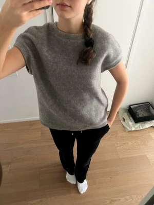 Grå kortärmad stickad tröja - Säljer en enkel och stilren grå stickad tröja med korta ärmar och rund hals. Tröjan har en rak passform och är gjord i ett mjukt material som känns skönt mot huden. Perfekt att matcha med både jeans och kjol.