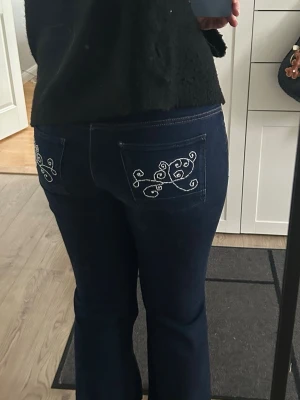Mörkblå bootcut jeans med brodyr - Snygga mörkblå jeans med bootcut passform och vita broderade detaljer på bakfickorna. Jeansen har klassisk femficksdesign och är tillverkade i ett mjukt denimtyg som sitter skönt. Perfekta för dig som vill ha en unik touch på din denimstil.             Det är bara att du skickar om du har några frågor☺️☺️