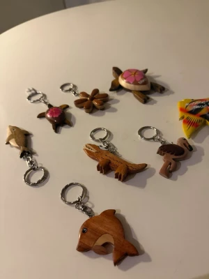 Handgjorda nyckelringar i trä - Säljer ett gäng handgjorda nyckelringar i trä med motiv som delfin, sköldpadda, blomma, fågel, fisk och krokodil. Fina detaljer och naturliga träfärger, vissa med målade inslag i rosa och gult. Perfekt accessoar för dig som gillar unika detaljer.