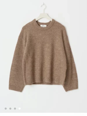 Beige stickad tröja med rund hals - Mysig beige stickad tröja med avslappnad passform och rund halsringning. Tröjan har långa ärmar och ribbade muddar vid ärmslut och nederkant. Perfekt för lager på lager och enkel att matcha med olika outfits.