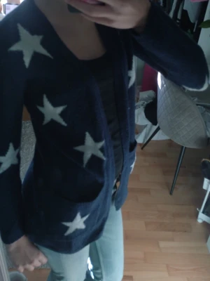 Mörkblå kofta med vita stjärnor - Snygg mörkblå kofta med stora vita stjärnor, öppen framtill och med två fickor. Perfekt för dig som gillar en avslappnad och trendig stil. Mjuk och skön stickad kvalitet som passar till jeans eller leggings.