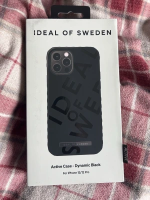 Svart mobilskal Ideal of Sweden iPhone 12 - Snyggt svart mobilskal från Ideal of Sweden, modell Active Case Dynamic Black. Passar iPhone 12 och 12 Pro. Skalet har en matt finish med stor logga och är gjort i tåligt material som skyddar mobilen mot stötar. Perfekt för dig som vill ha ett stilrent och funktionellt skal. Helt nytt oanvänt skal, obruten förpackning