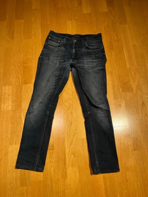 Nudie Lean Dean Jeans - Snygga mörkblå slim fit jeans med diskreta slitningar och klassisk femficksmodell. Jeansen har normal midja och raka ben. Perfekta för en avslappnad och trendig look. Materialet är troligtvis bomull med lite stretch för extra komfort.