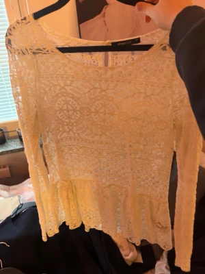 Vit spetsblus från Gina Tricot - Säljer en vit långärmad spetsblus från Gina Tricot med vackra broderade detaljer och volang nedtill. Blusen är genombruten och har rund halsringning, perfekt för dig som gillar romantisk stil.