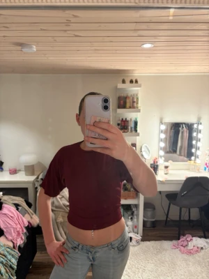 Vinröd croppad topp från 157 - Säljer en vinröd croppad topp från 157. T-shirten har korta ärmar och en tight passform som framhäver midjan. Perfekt att matcha med  jeans eller kjol. Enkel och stilren design utan mönster.