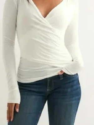 Vit omlottopp med v-ringning - Snygg vit omlottopp med v-ringning och långa ärmar. Toppen har en figurnära passform och är perfekt att styla med jeans eller kjol. Enkel men stilren design som passar till många olika looks.