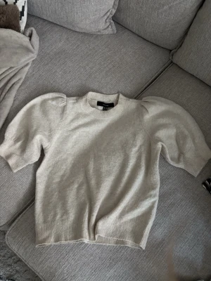 Beige puffärm tröja från Vero Moda - Snygg beige tröja från Vero Moda med puffärmar och ribbade muddar. Tröjan har rund halsringning och är gjord i mjukt stickat material, perfekt för en trendig och avslappnad look.