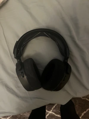 SteelSeries svarta gaminghörlurar - Säljer ett par svarta over-ear gaminghörlurar från SteelSeries. De har en bred, vadderad huvudbygel med tygband och stora, mjuka öronkuddar i tyg. Hörlurarna har knappar och portar på ena kåpan och en stilren, matt finish.