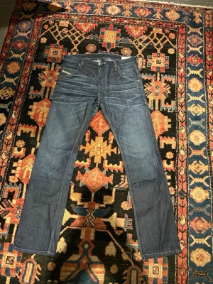 Mörkblå raka jeans Från Diesel - Snygga mörkblå jeans med raka ben och klassiska fem fickor. Jeansen har ljusa sömmar och diskreta slitningar framtill för en cool look. Passar perfekt till en avslappnad stil. Materialet är denim.