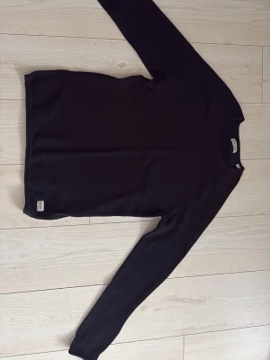 Svart stickad tröja Jack & Jones - Snygg svart stickad tröja från Jack & Jones med rund halsringning och lång ärm. Tröjan har en diskret etikett nertill och är gjord i ett mjukt, strukturerat material som passar perfekt till alla outfits.