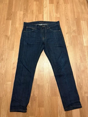 Nudie jeans Selvedge  - Säljer ett par mörkblå jeans från Nudie Jeans med klassisk femficksmodell och raka ben. Jeansen har kontrastsömmar och Nudie-logga på bakfickan. Tillverkade i kraftig denim som ger en snygg och tidlös look,Model Lean Dean 