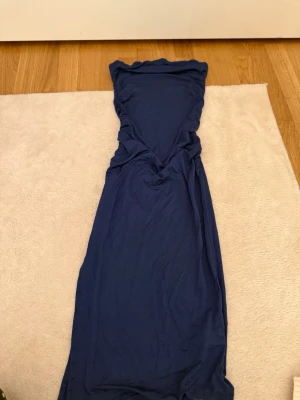 Blå långklänning i mjukt tyg - En stilren blå långklänning med enkel design och mjukt fallande material. Klänningen har en figurnära passform upptill och är ärmlös, perfekt för en elegant look.