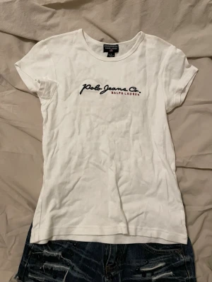 Vit Polo Jeans Co. t-shirt Ralph Lauren - Klassisk vit t-shirt från Polo Jeans Co. Ralph Lauren med broderad logga i marinblått och rött på bröstet. T-shirten har rund halsringning och korta ärmar. Tillverkad i mjuk bomull som känns skön mot huden.