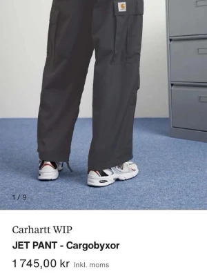 Carhartt cargobyxor - Mörkgrå cargobyxor från Carhartt WIP med bred passform och flera stora fickor på sidorna. Byxorna har knappt används och är tillverkade i slitstarkt bomullstyg. Köpta för ca 1800 och säljs för halva priset. 