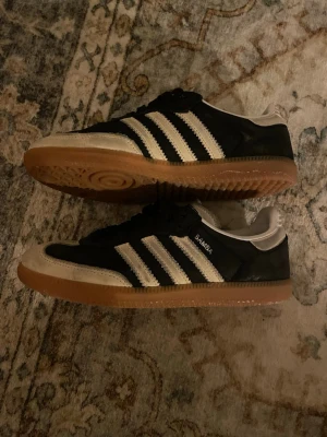 Adidas Samba svart/vit sneakers - Klassiska Adidas Samba sneakers i svart med vita detaljer. Storlek 38 Skon har vit tå och häl, samt brun gummisula för extra grepp. Perfekt för dig som gillar retrostil och streetwear. Dom är smutsiga men är i bra skick och har inga övriga tydliga skador. Nypris 1200kr