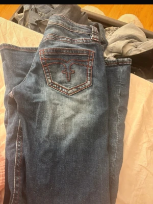 Blå jeans från Gina Tricot XS - Snygga blå jeans från Gina Tricot i storlek XS. Jeansen har röda kontrastsömmar och en unik broderad bakficka. Klassisk femficksmodell med dragkedja och knapp. Perfekta till en avslappnad look och passar till det mesta.