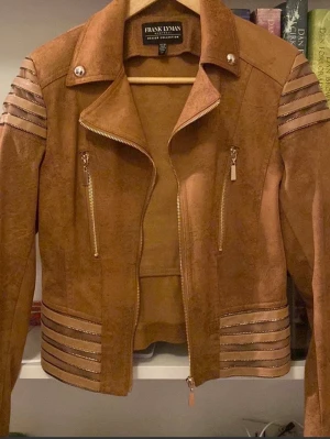 Brun mockajacka från Frank Lyman - Säljer en snygg brun mockajacka från Frank Lyman med coola detaljer i form av ränder på ärmar och nederkant. Jackan har dragkedjor framtill och på fickorna samt en klassisk krage. Perfekt för dig som vill sticka ut lite extra.