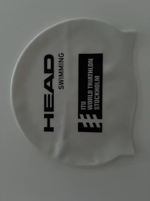 Vit badmössa HEAD ITU Stockholm - Säljer en vit badmössa från HEAD med svart tryck 'ITU World Triathlon Stockholm'. Tillverkad i stretchigt material som sitter tajt på huvudet och passar perfekt för simning och triathlon. Onesize. Ny.