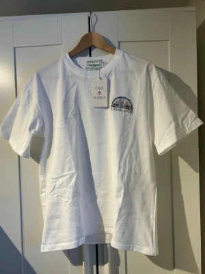 Vit t-shirt från Casablanca - Vit t-shirt från Casablanca med tryck på bröstet och stort färgglatt motiv på ryggen. Klassisk passform med rund hals och korta ärmar. Perfekt för dig som gillar stilrena plagg med snygga detaljer. Helt ny priset kan diskuteras 