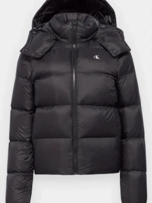 Svart pufferjacka från Calvin Klein - Snygg svart pufferjacka från Calvin Klein med huva och diskret CK-logga på bröstet. Jackan har en hög krage, dragkedja framtill och quiltad design. Tillverkad i ett glansigt material som ger en modern look och håller dig varm under kalla dagar.