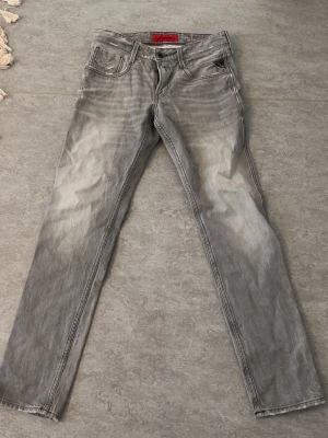  Replay anbass  - Snygga gråa jeans från Replay med raka ben och klassisk femficksmodell. Jeansen har slitna detaljer och en tvättad look som ger en cool vibe. Tillverkade i mjukt denimtyg som är skönt att bära. Perfekta för dig som gillar en avslappnad men trendig stil.