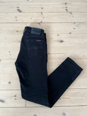 Svarta slim jeans från Nudie - Säljer ett par svarta slim fit jeans från Nudie Jeans. Modellen är Lean Dean och de är inorincip nya använda ett fåtal gånger utan hål eller defekter. Klassisk femficksmodell med svarta sömmar och diskret logga på bakfickan. Jeansen har normal midja och raka ben. Materialet är mjukt och stretchigt för extra komfort. Vid frågor eller funderingar är det bara att säga till Mvh Olof.