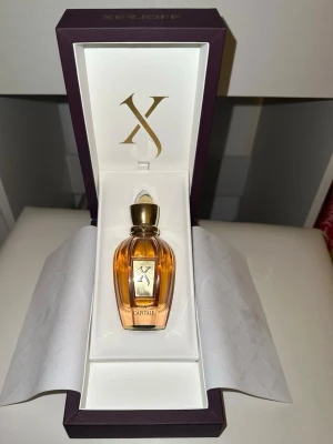 Xerjoff La Capitale parfym - Lyxig parfym från Xerjoff i modellen La Capitale. Flaskan är elegant med guldiga detaljer och genomskinligt glas som visar den bärnstensfärgade vätskan. Kommer i en exklusiv lila och vit presentask med guldfärgad logotyp. Jättefin doft men för stark för min smak.