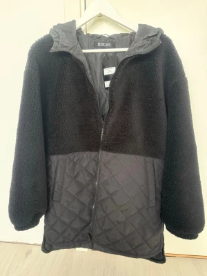 Svart teddyjacka med huva från Noisy May - Säljer en svart teddyjacka från Noisy May med huva och dragkedja. Överdel i mjukt teddy-material och nederdel i quiltat tyg. Jackan har en oversized passform och är perfekt för kalla dagar. Enkel och stilren design som passar till det mesta.