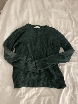 Mörkgrön stickad tröja - Mysig mörkgrön stickad tröja med rund halsringning och långa ärmar. Tröjan är lite nopprig annars i fint skick 